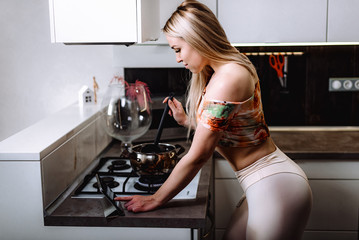 Beautiful sporty girl uses a digital tablet and cooks leaning on a table in the kitchen