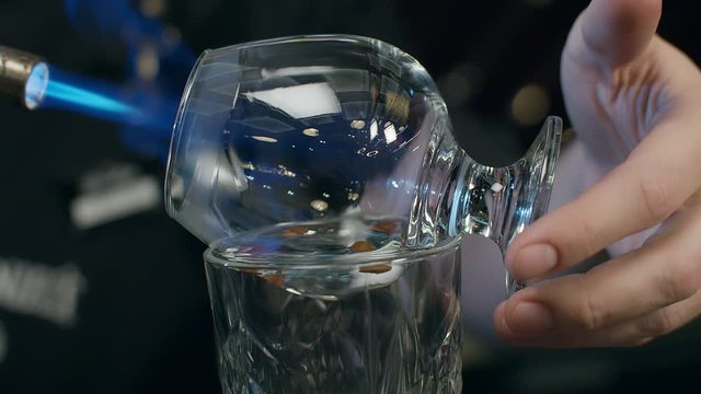 the barman sets fire to a sambuca with coffee grains, rotates the glass with his hand