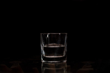 A glass half filled with water placed on a glass plate in a dark copy space background.