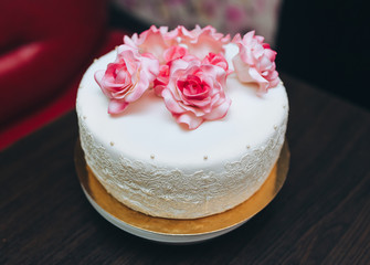 A single tier white wedding cake with pink rose flowers from a pastry glaze. Handmade holiday sweets.