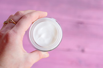 A woman's hand with a jar of face cream on a pink background. The concept of cosmetics.