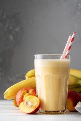 Fresh protein shake with nectarine or peach on a white wooden table. Fresh apricot milkshake. A glass of banana smoothie.