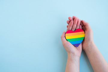 Womans hands hold heart in the colors of rainbow on light blue background. LGBT concept, Pride month. Top view, copy space - obrazy, fototapety, plakaty