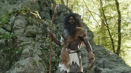 First human african hunter-gatherer in animal fur walking on rocks mountain in jungle forest feeling freedom and pride. nomadic tribesmen of neanderthals.