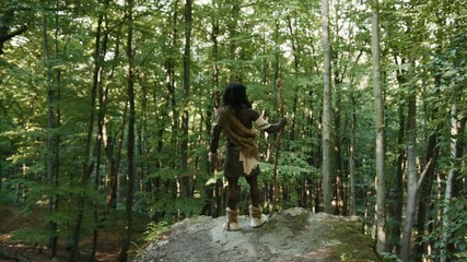 Proud wildman of neanderthals on edge of rock enjoying freedom and glory hands to the side. Caveman leader of nomadic tribe walking in jungle forest. Homo sapiens.