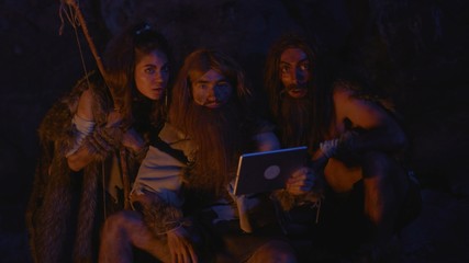 Prehistoric tribe family using future tablet computer at night. Wild people aborigines noticing...