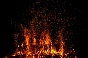 A burning log in a fire with multiple sparks in the night darkness