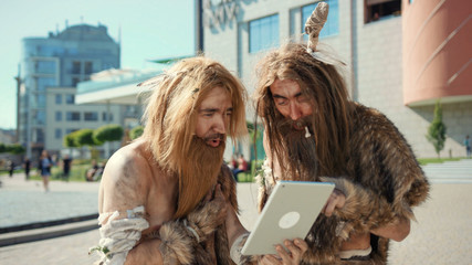 Ancient wild homo sapiens rejoicing with new toy technology digital tablet outdoors. Primitive...