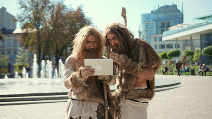 Modern-day neanderthals using digital tablet in present city. Archaic smart cavemen browsing...