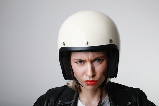 Portrait of biker young woman, with serious face, wearing white helmet, with red lips. Studio background.