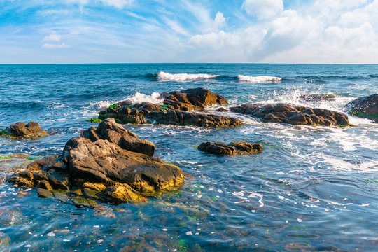 rocky shoreline of the sea in the morning. beautiful scenery with splashing waves and clouds on the sky. calm summer weather