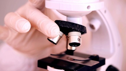 Focus on a microscope handling by a person with white latex gloves