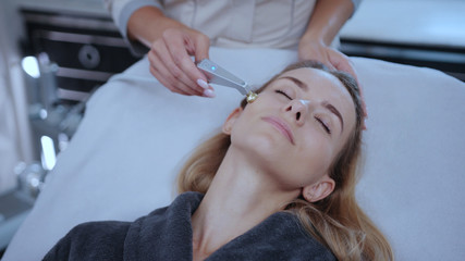Obraz na płótnie Canvas Head of beautiful woman receiving skin healh care facial treatment in spa salon. Close-up beautician rf-lifting customer face skin with modern hardware cosmetology.