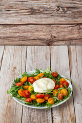 Tasty, fresh salad with mozzarella burrata, arugula, cherry tomatoes and basil on a white plate on a wooden background.Close up. Healthy Italian food. Selective focus