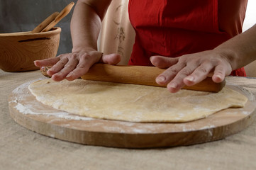Women's hands roll out the dough with a rolling pin on the table.