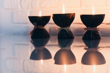 Burning spa aroma candles in coconut shell on a glass white table, cozy home interior.