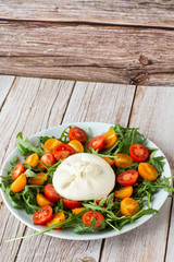 Tasty, fresh salad with mozzarella burrata, arugula, cherry tomatoes and basil on a white plate on a wooden background.Close up. Healthy Italian food. Selective focus