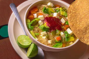 Caldo tlalpeño servido con tostada y limones