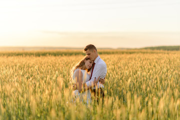 Naklejka na ściany i meble Bride and groom in a wheat field. A couple is hugging during sunset.