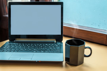 Computer and a cup of hot beverage against the window with raindrops background. Copy space.