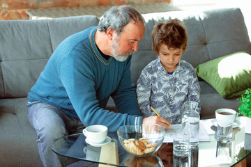 Useful time. Grandfather and his grandson spending time together insulated at home. Having fun, stadying, reading and drawing. Concept of quarantine, family, love, realtions, togetherness, education.