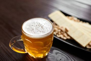 Mug of unfiltered light wheat beer with beer snacks on wooden table