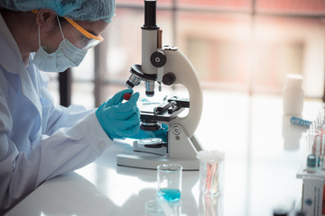 Scientist hold pipette adding fluid to test on microscope with copy space using as background...
