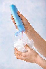 Female hands with shower gel and loofah on light background