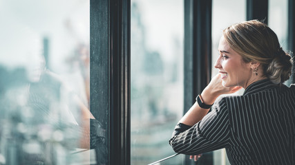 Portrait of sophisticated young successful confident CEO businesswoman looking out at the city from...