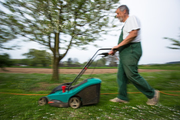 Gardener mowing the lawn - motion blurred image (color toned image)