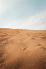 Beautiful landscape of desert with dunes and blue cloudy sky on backround. Footsteps in orange dunes.