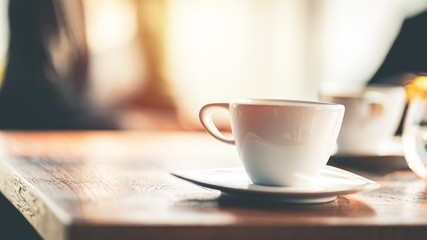 A white ceramic coffee cup with saucer on the wooden table indoors.	