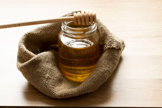 jar of honey in a sackcloth bag. on top of the jar lies the Honey Dipper for honey.