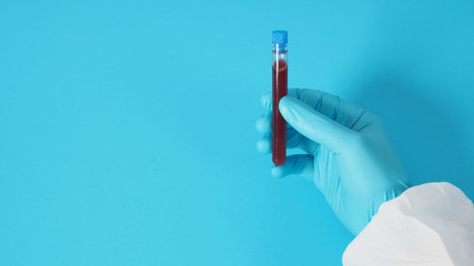 model with PPE suite and Hand with glove is holding blood test tube on blue background.