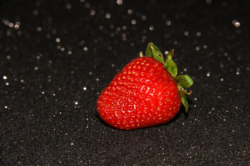 One strawberry on a black background with sequins. Red berry.