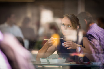 Pretty, young woman eating sushi in a restaurant, having her lunch break, enjoying the food, pausing for a while from her busy corporate/office life (color toned image)
