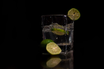 Water splashes out of the garnished glass as a green fresh lemon slice immerses into the water.