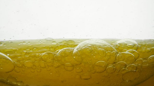 Large and small air bubbles on the surface of delicious corn and soybean oil, close-up shots. A beautiful golden liquid mixes slightly with water in a circle and a structure of air drops appears.