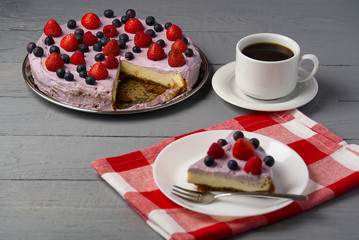 Piece of home made Cheesecake with berries on plate and mug of Americano coffee. Cheesecake with Strawberry, blueberry and raspberry on grey wooden background.