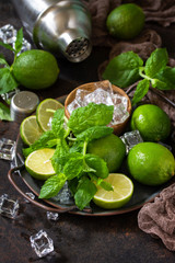 Refreshing Mojito cocktail making. Mint, lime, ice ingredients and bar utensils on a dark stone background.
