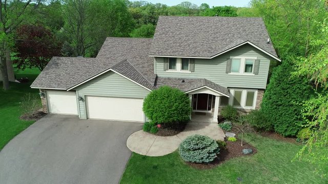 Drone aerial of a middle class suburban American home with typical modern design, a nice lawn and garage, filmed on a sunny summer or spring day.