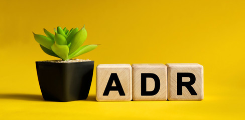 ADR - financial concept on a yellow background. Wooden cubes and flower in a pot.