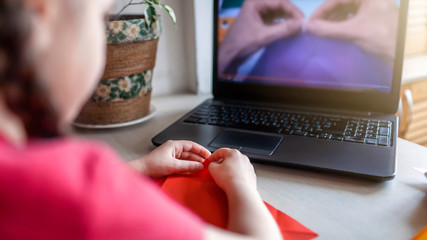 Girl doing origami fish with color paper looking video on laptop, online workshop and distant...