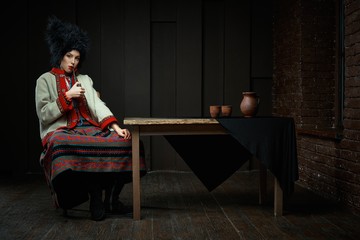 Gorgeous young woman in ukrainian traditional costume smoking pipe. Portrait of attractive woman in hat with red lips.