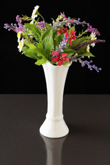 Artificial flowers in a white vase. A bouquet of artificial flowers in a white vase on a black background.