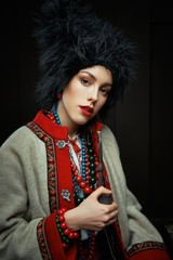 Gorgeous young woman in ukrainian traditional costume smoking pipe. Portrait of attractive woman in hat with red lips.
