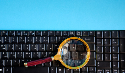 Golden magnifying glass on a black keyboard on a blue background with copy space