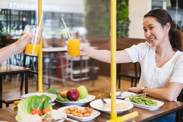Asian woman sitting in restaurant eating food with table shield to protect infection from coronavirus covid-19, restaurant and social distancing concept