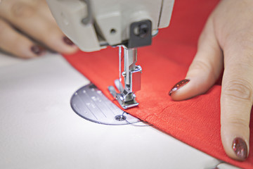 The master sews on a sewing machine. The master is sewing red fabric on a sewing machine. Closeup