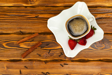 black coffee in whute cup with strawberry, cinnamon and spices on a wooden red table